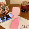 A pink adjustable foldable phone and tablet stand resting on a wooden table next to a glass of iced tea.
