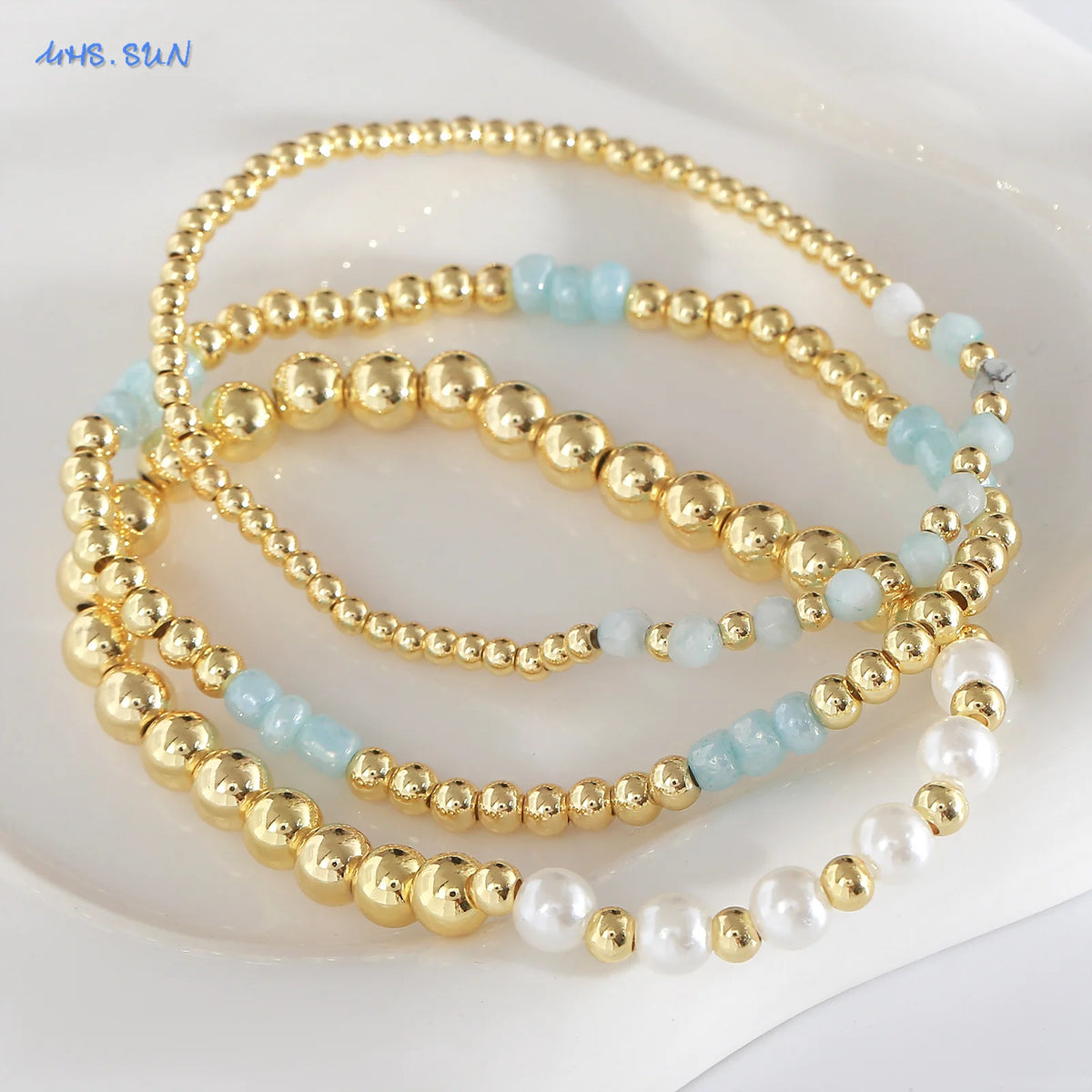 Gold-plated shell pearl beaded bracelets in various shades of blue and white displayed on a white background.