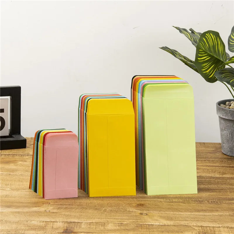 Une collection d'enveloppes en papier colorées dans différentes nuances de rose, jaune et vert sont présentées sur une surfac