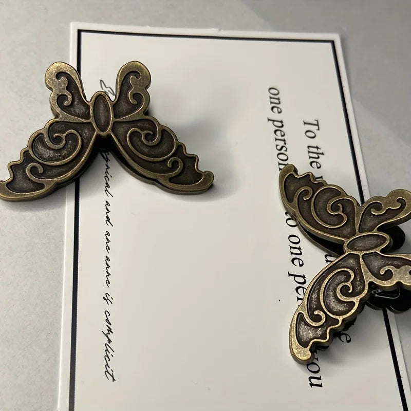 A vintage butterfly metal book clip with an ornate design is shown against a white card.