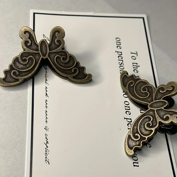 A vintage butterfly metal book clip with an ornate design is shown against a white card.