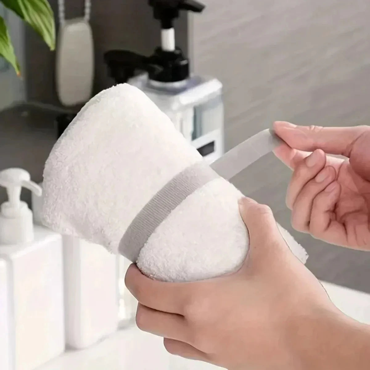 A hand is holding a white, fluffy sponge or cleaning pad with a gray hook and loop strap.