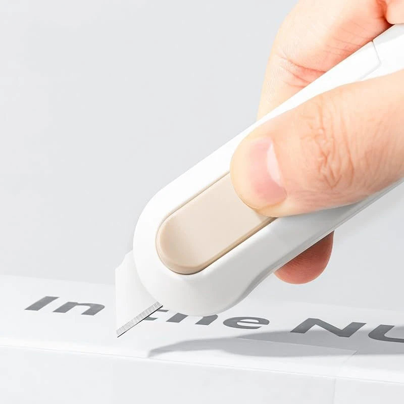 A hand is operating a white portable mini paper cutter on a white box.
