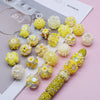 A collection of yellow and clear acrylic flower beads for jewelry making displayed on a white surface.
