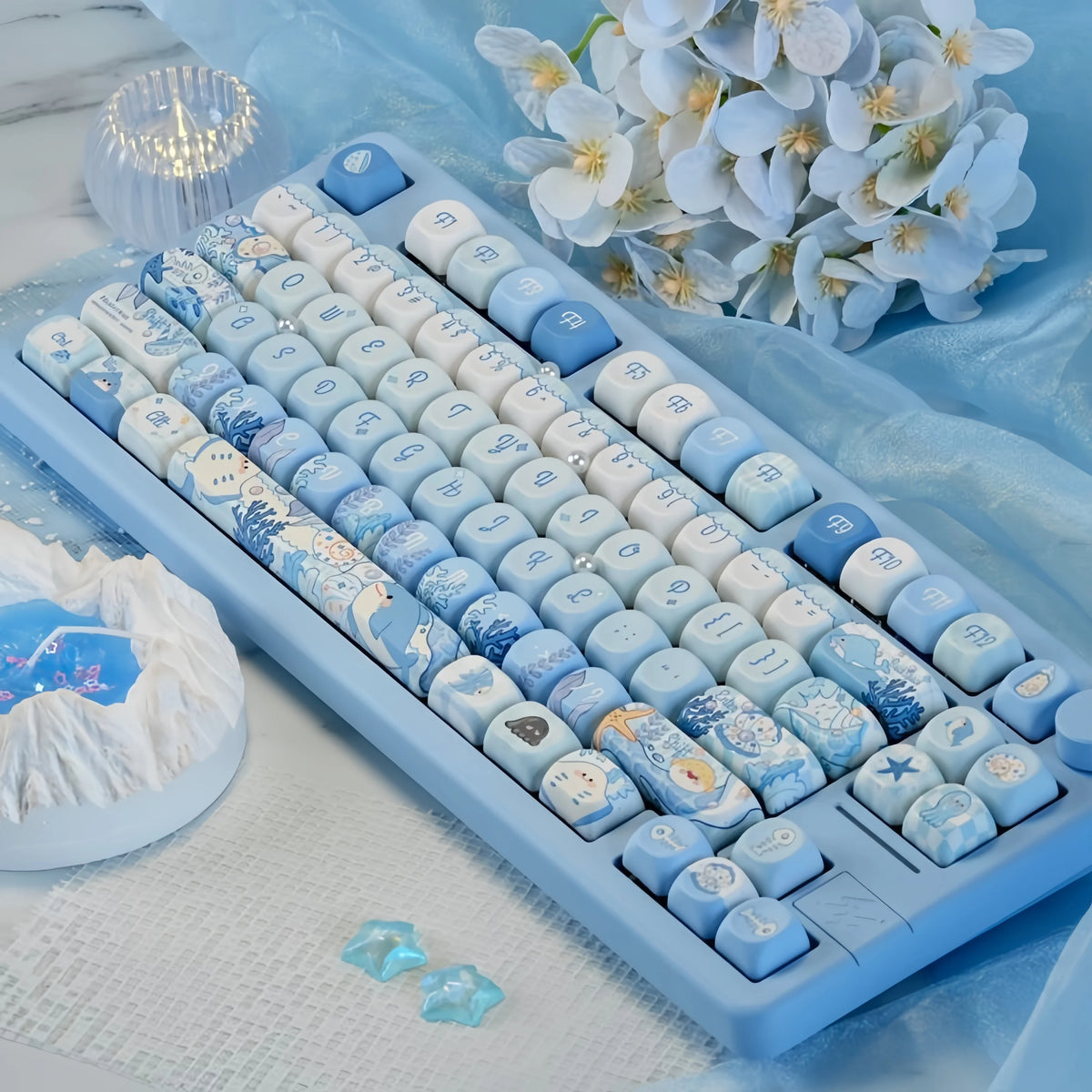 A close-up of blue sea themed PBT keycaps for a mechanical keyboard displayed on a light blue cloth.