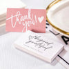 Pink and white thank you cards with handwritten messages on a white surface.