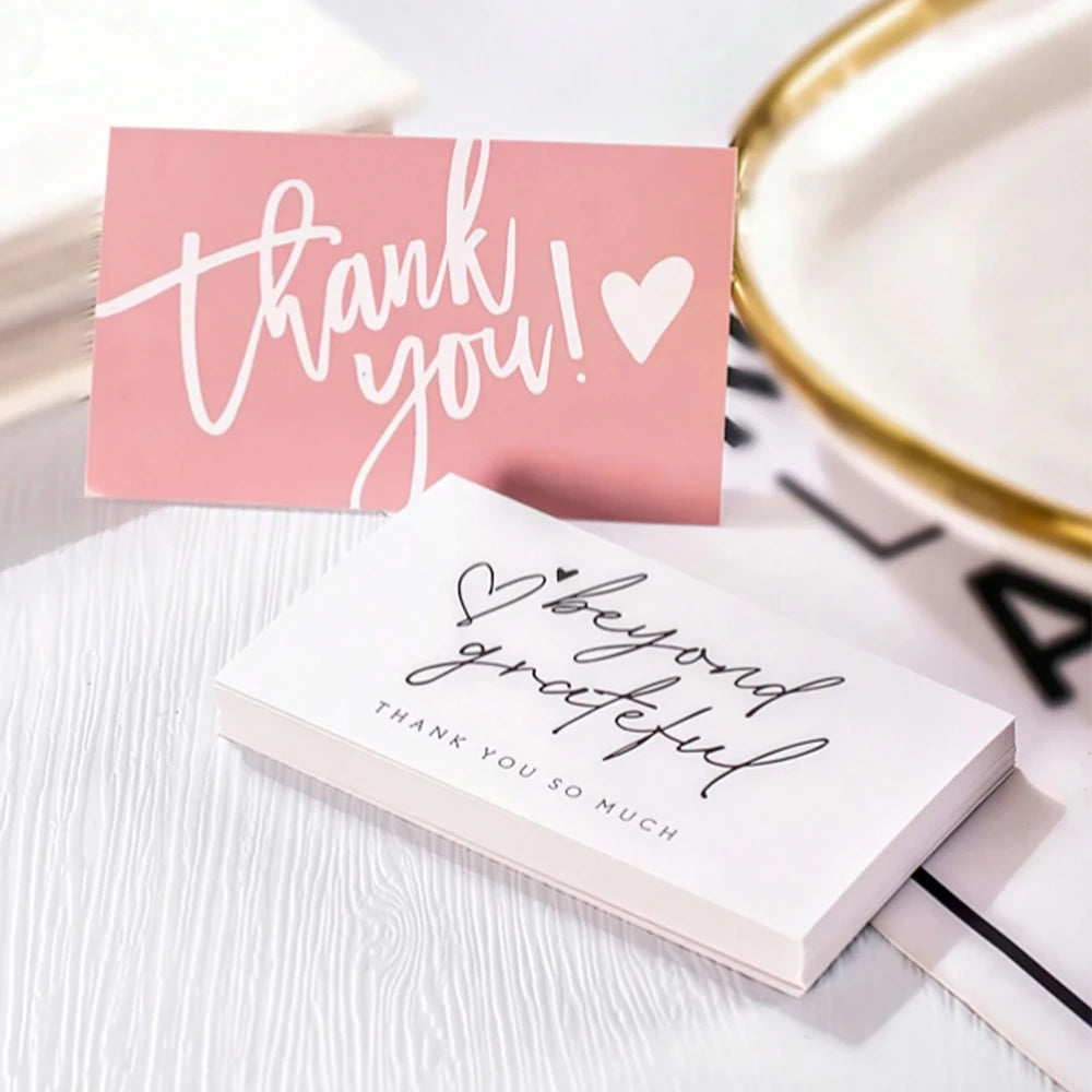 Pink and white thank you cards with handwritten messages on a white surface.
