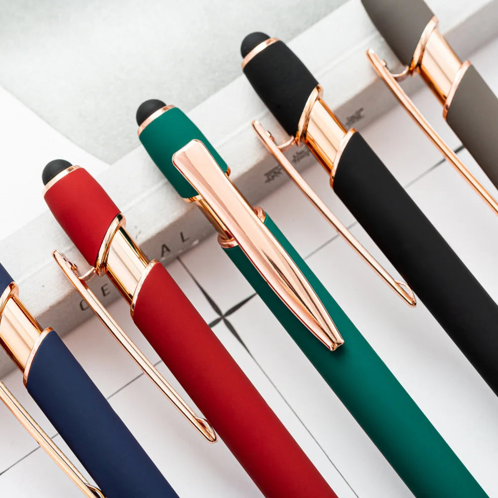 A collection of black and gold retractable stylus and ballpoint pens arranged diagonally on a white surface.