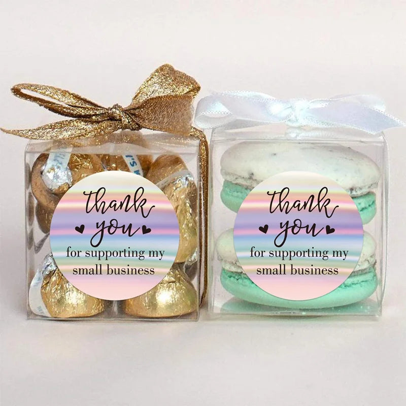 A clear plastic package of rainbow laser thank you stickers with gold foil accents and a light blue ribbon.