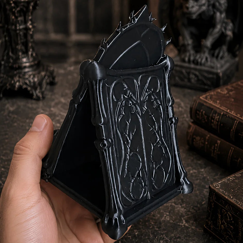 A hand holds an open black gothic skull phone stand with intricate carvings.