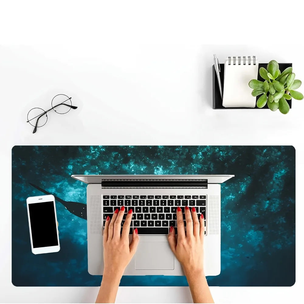 A person's hands are using a laptop on an ocean-themed mouse pad featuring a whale shark design.