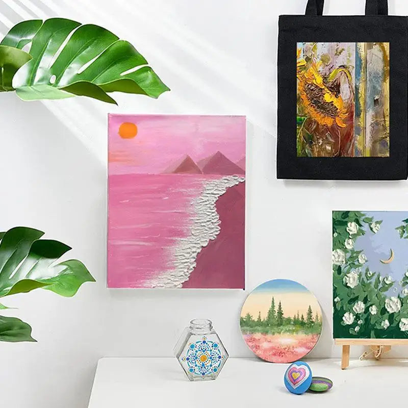 Set Acrylfarbstoffe für Stoff und Leder DIY, neben einer schwarzen Tasche und einem rosa Landschaftsbild.