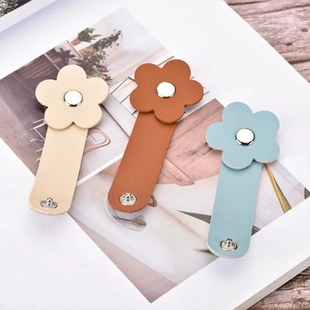Three leather flower cable organizers in beige, brown, and mint green are displayed on a wooden surface.