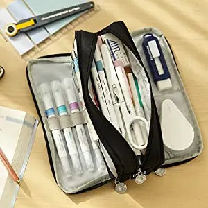 A black fabric pencil pouch with a clear compartment holding various pens and pencils is shown on a wooden surface.