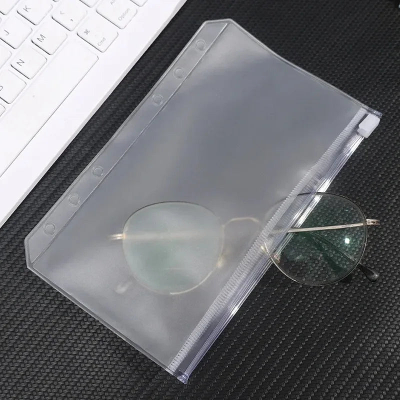 A clear PVC zipper binder pocket containing eyeglasses and other small items on a dark surface.