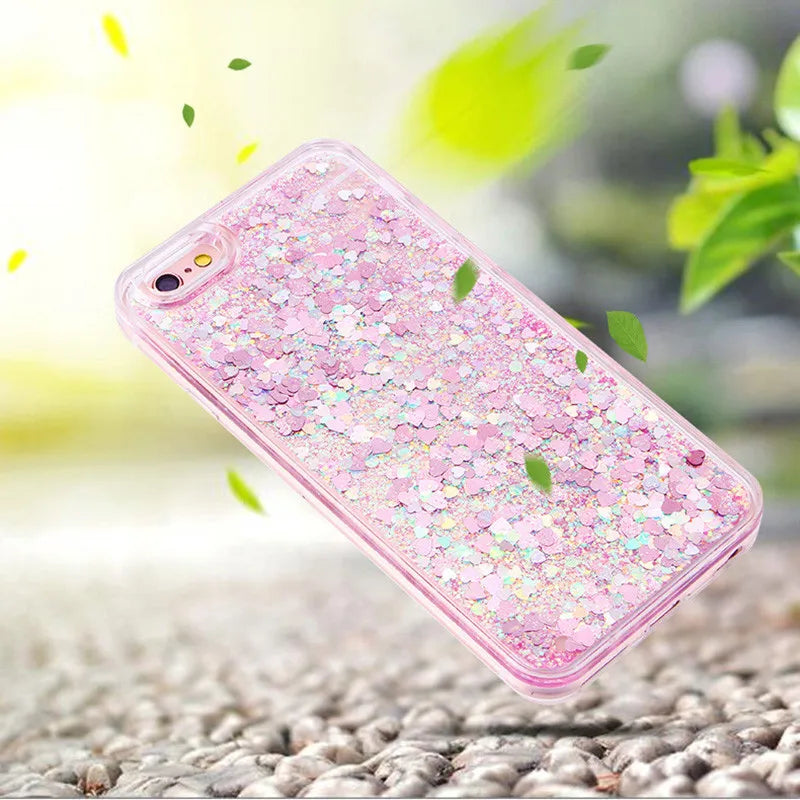A pink glitter heart star liquid phone case is shown lying on a surface with green leaves in the blurred background.