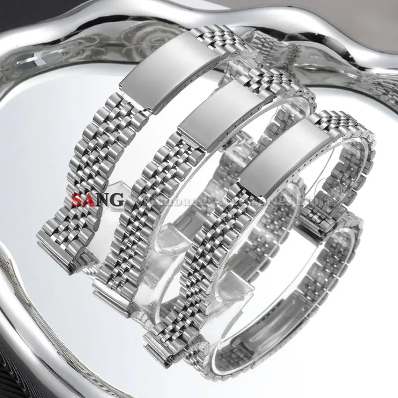 A close-up view of a polished stainless steel watch band with a folding clasp displayed on a reflective surface.