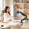 A woman is using a fully adjustable monitor arm for desktops on a white desk in a bright office setting.