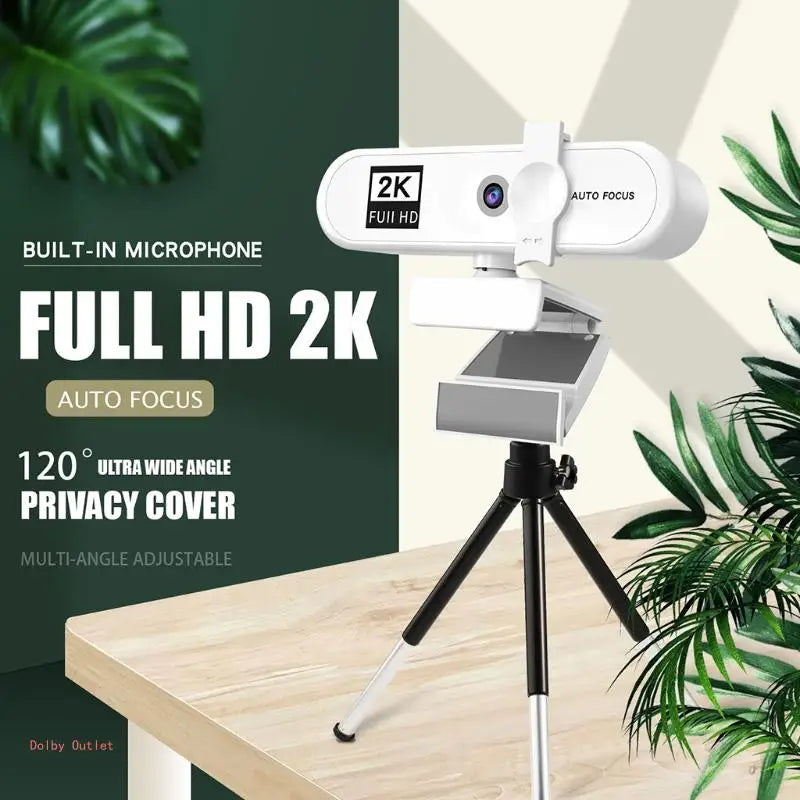 Webcam 2K Full HD blanche avec autofocus montée sur trépied, devant un fond de plantes vertes floues.