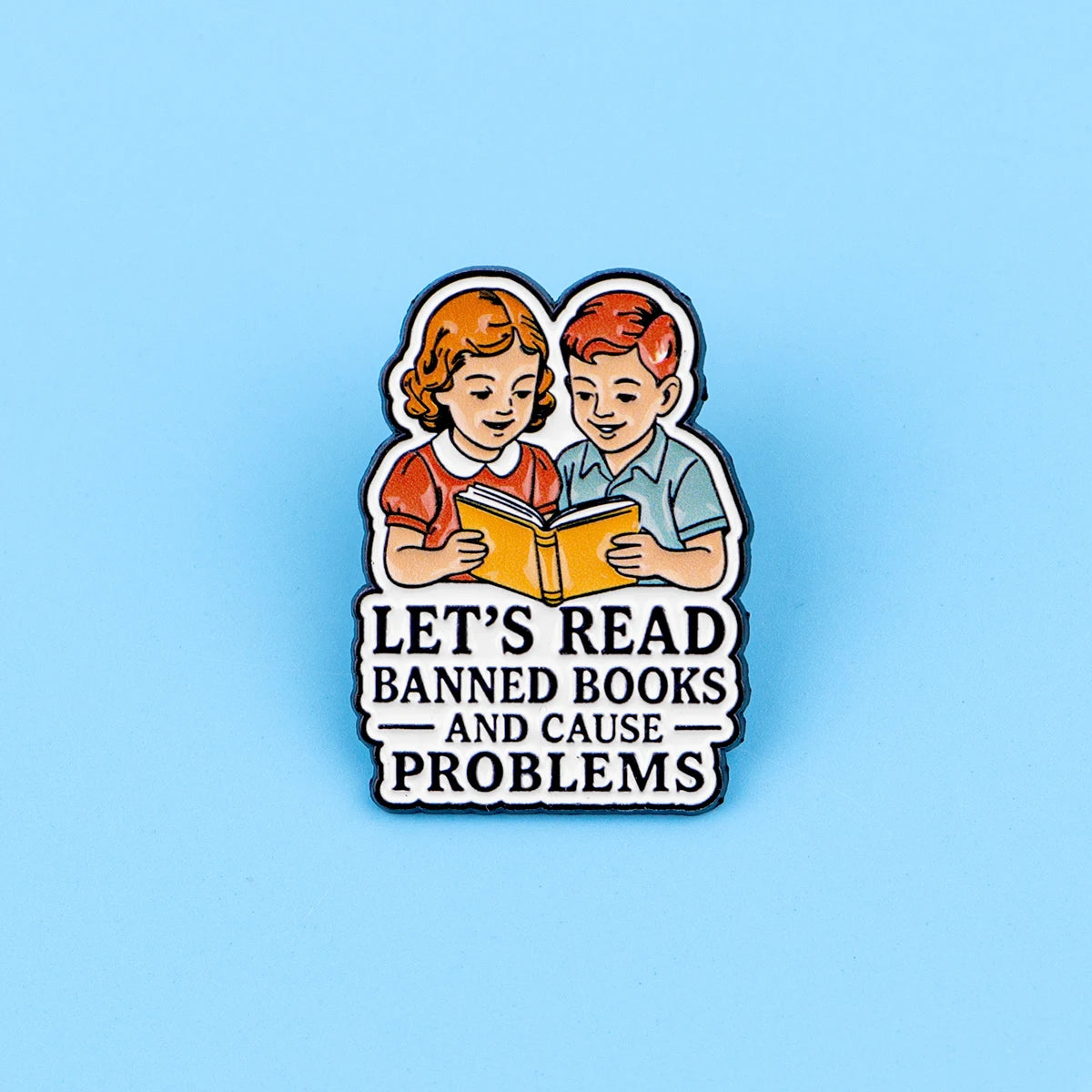 An enamel lapel pin featuring two children reading a book with the text Let's Read Banned Books and Cause Problems