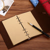 Un cuaderno encuadernado en cuero marrón con una página color canela y un bolígrafo negro sobre una superficie de madera.