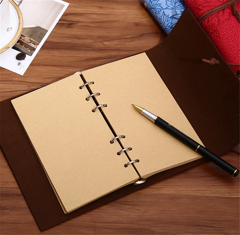 Un cuaderno encuadernado en cuero marrón con una página color canela y un bolígrafo negro sobre una superficie de madera.