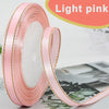 Roll of light pink satin ribbon with gold edges displayed next to a piece of fabric.