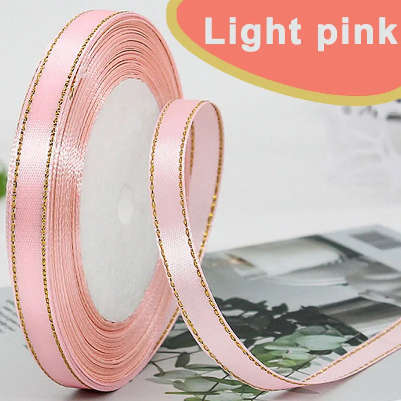 Roll of light pink satin ribbon with gold edges displayed next to a piece of fabric.