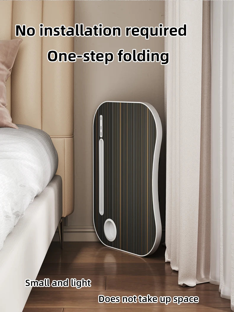 A sleek, folding laptop desk organizer tray in black and gold is shown next to a bed and curtains.