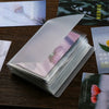 A stack of clear photo storage booklets featuring soft pink and white floral designs on a dark wooden surface.