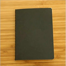 Un carnet à dessin A6 noir et vierge posé sur une surface en bois.