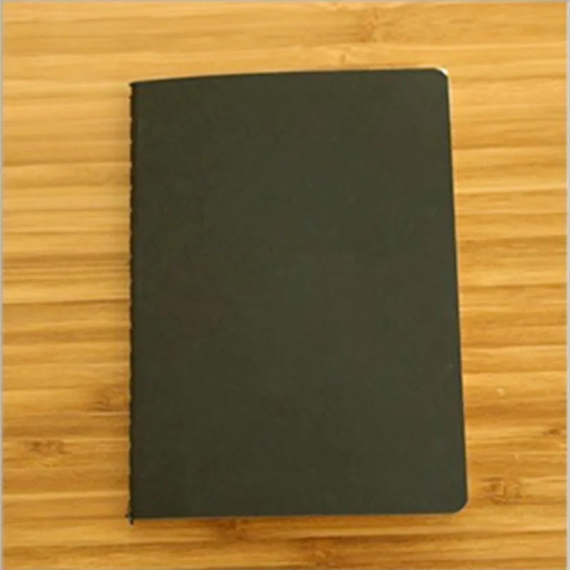 A black A6 blank sketchbook lying on a wooden surface.