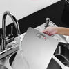 Hands are cleaning a stainless steel cutting board inside a kitchen sink.