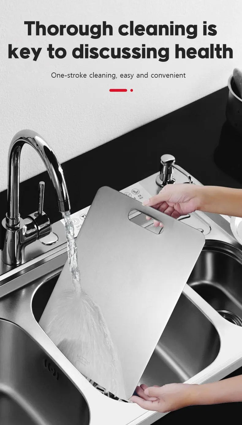 Hands are cleaning a stainless steel cutting board inside a kitchen sink.
