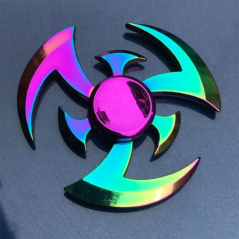 A rainbow metal fidget spinner with iridescent, multicolored blades resting on a dark gray surface.