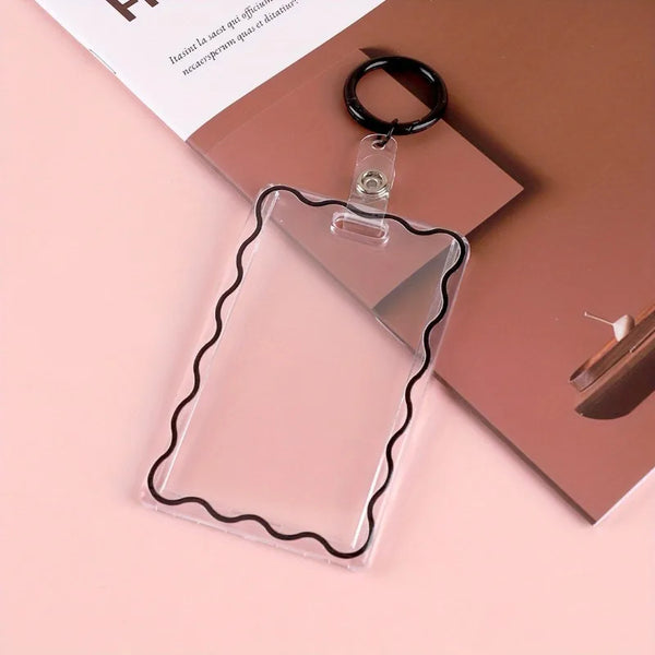 A clear acrylic card holder with a decorative border is displayed next to a black key ring on a pink background.