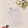 A clear acrylic card holder with a decorative border and attached to a key ring is shown on a light surface.