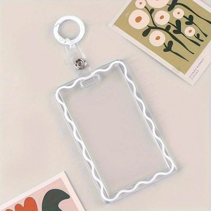 A clear acrylic card holder with a decorative border and attached to a key ring is shown on a light surface.