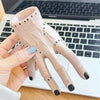 A hand wearing a light pink resin palm decoration with black nail tips is held over a laptop keyboard.