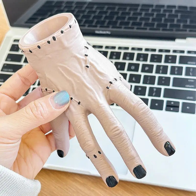 A hand wearing a light pink resin palm decoration with black nail tips is held over a laptop keyboard.
