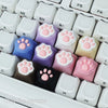 A collection of pink and purple kawaii cat paw and heart keycaps for MX switches arranged in a white tray.