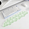 A light green, elongated cloud-shaped wrist rest for a keyboard and mouse is displayed on a white desk.