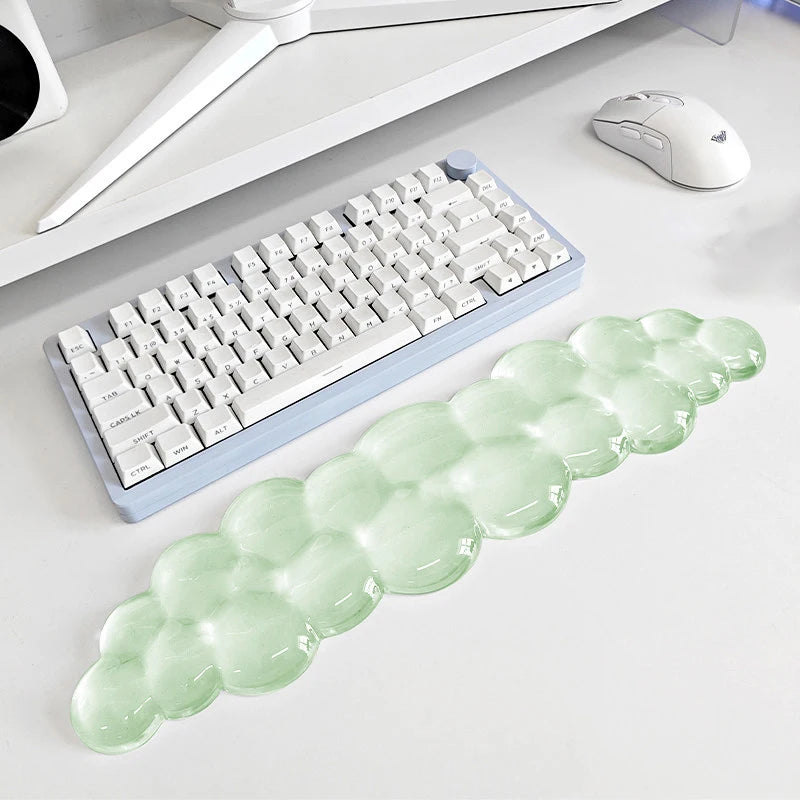 A light green, elongated cloud-shaped wrist rest for a keyboard and mouse is displayed on a white desk.
