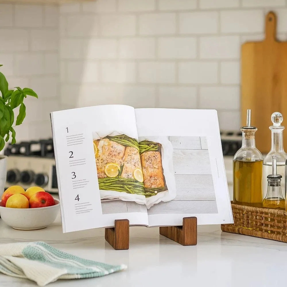 A vintage wooden cookbook holder stands on a counter, displaying an open recipe book with food photography.