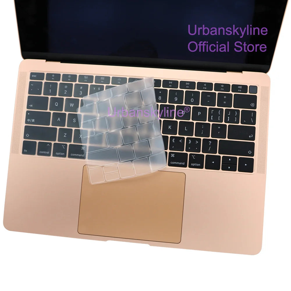 Una funda de teclado de silicona para MacBook, mostrada sobre una laptop rosa claro y un teclado transparente de silicona.