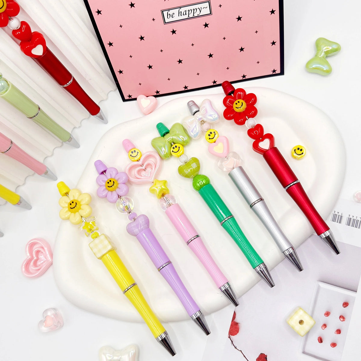 A set of colorful beaded ballpoint pens arranged on a white plate with a pink background.