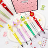 A set of colorful beaded ballpoint pens arranged on a white plate with a pink background.