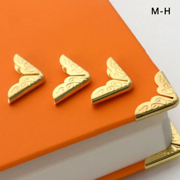 Three gold vintage metal book corner protectors placed on an orange book.