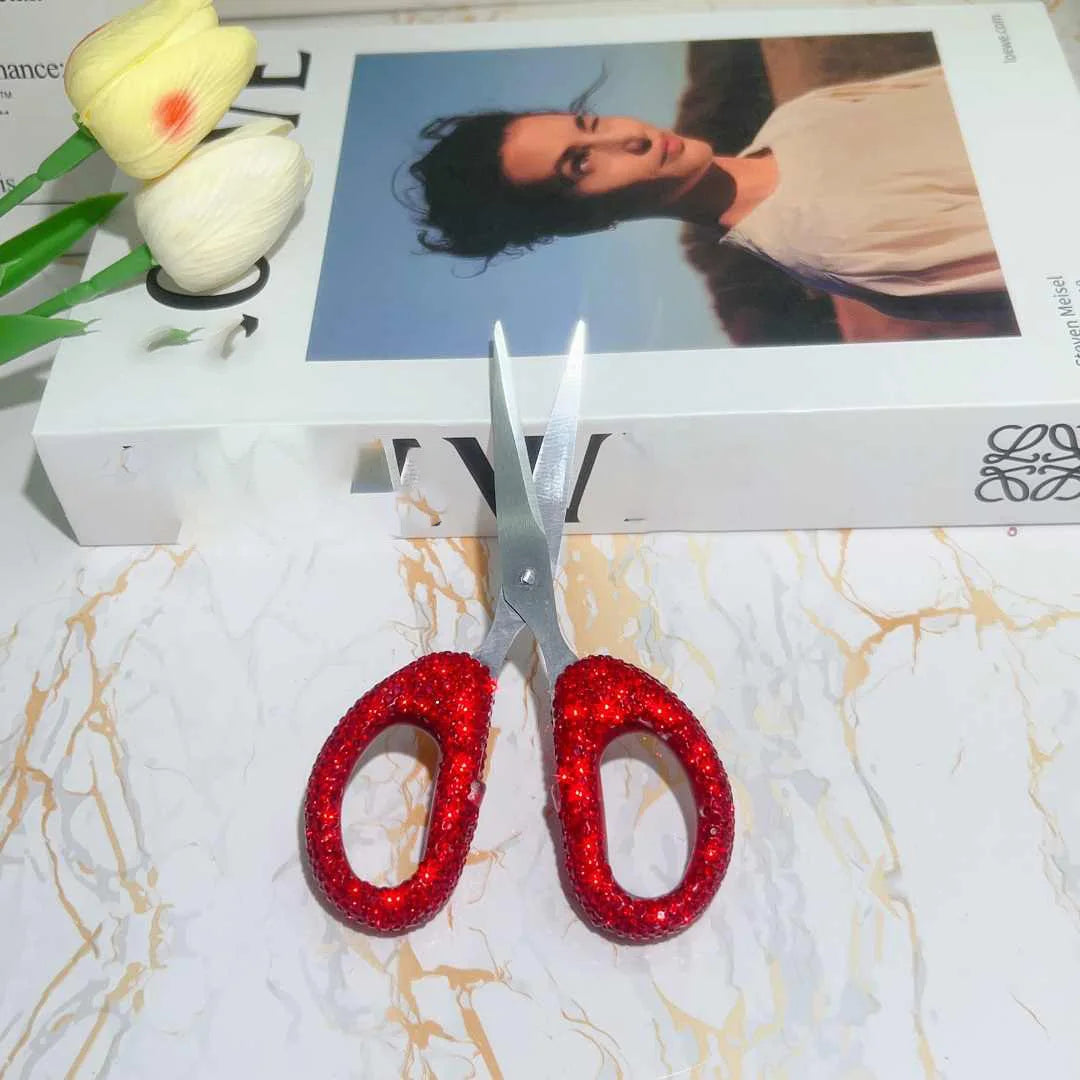 A pair of red rhinestone crafting scissors resting on a white surface next to a box.