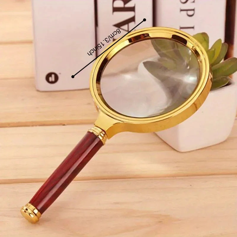 A gold-framed magnifying glass with a reddish wooden handle is shown next to a white object.